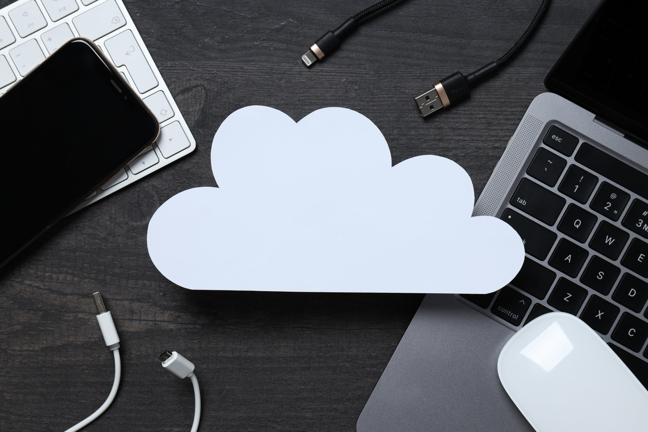 Imagem capa do conteúdo sobre StackSpot Cloud Service, onde há uma nuvem de papel branca ao centro, atrás está uma mesa com teclado de notebook e cabos de computador.