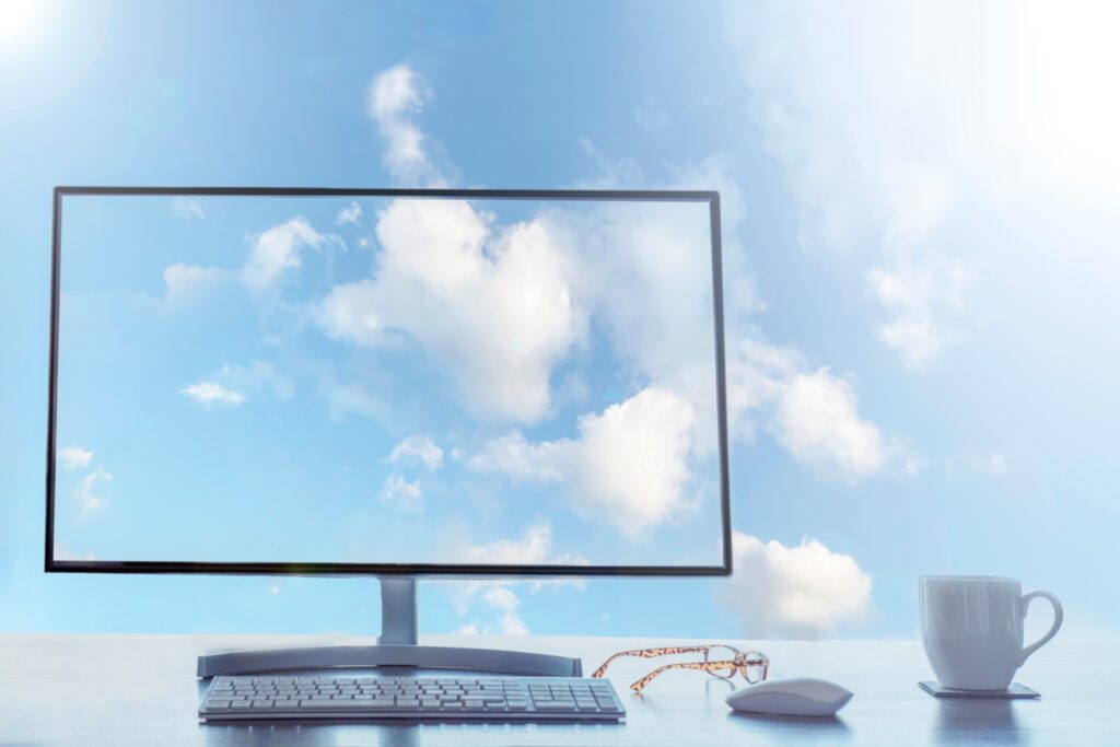 Capa do artigo “Migração para a nuvem: como implementar um plano de sucesso?” onde vemos um monitor de computador transparente em cima de uma mesa com teclado, mouse e um par de óculos. No fundo da imagem vemos um céu com nuvens, exibido também no monitor.