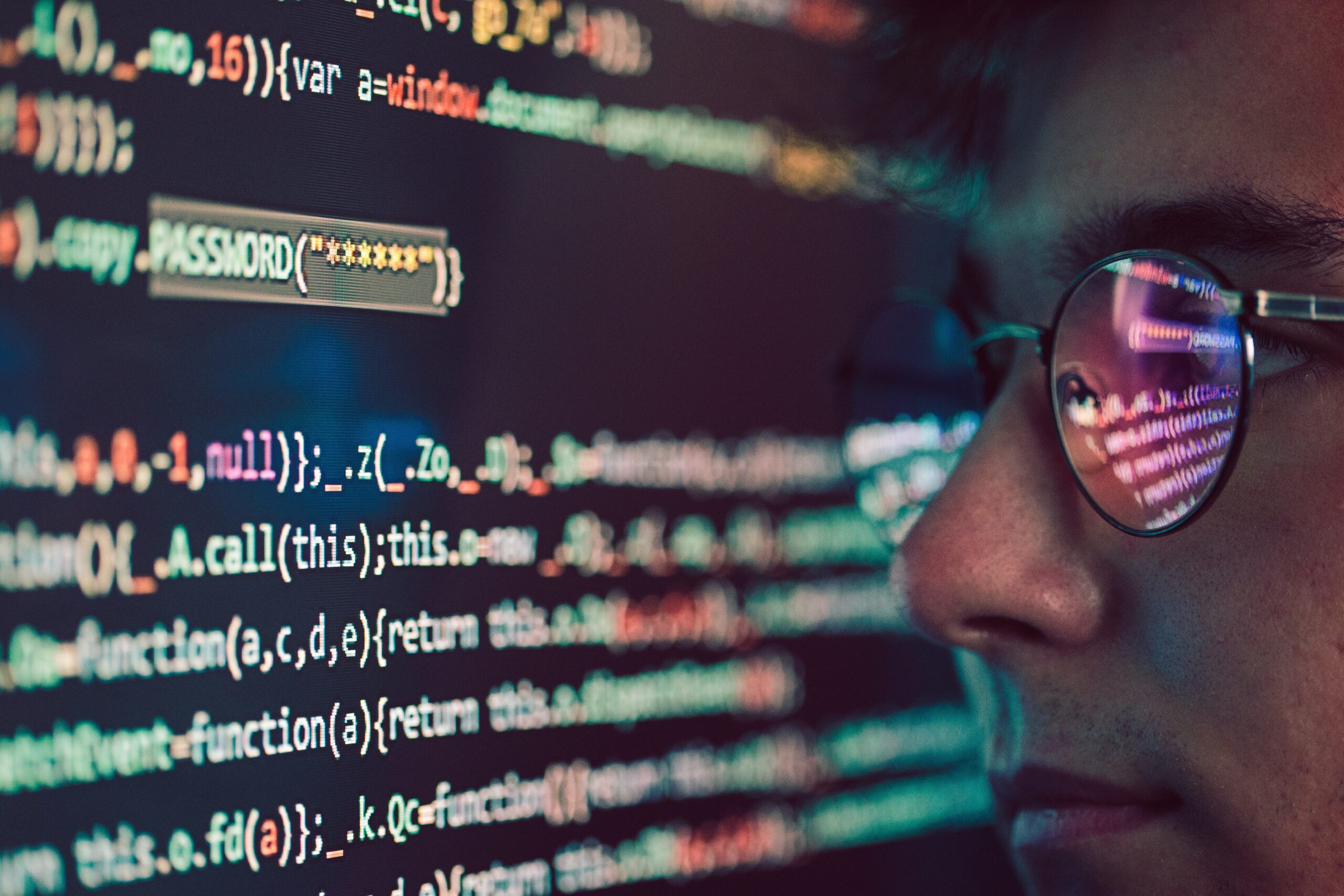 A white man with glasses looking at a computer screen with programming codes.