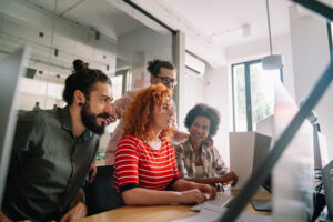 Article cover Inner Source: Concept, Benefits, and How to Implement it with four people huddled in front of a monitor in an office. The group is made up, from left to right, of a white man with brown hair and beard, a white woman with curly red hair, another white man with brown hair and a black woman with short, curly hair.