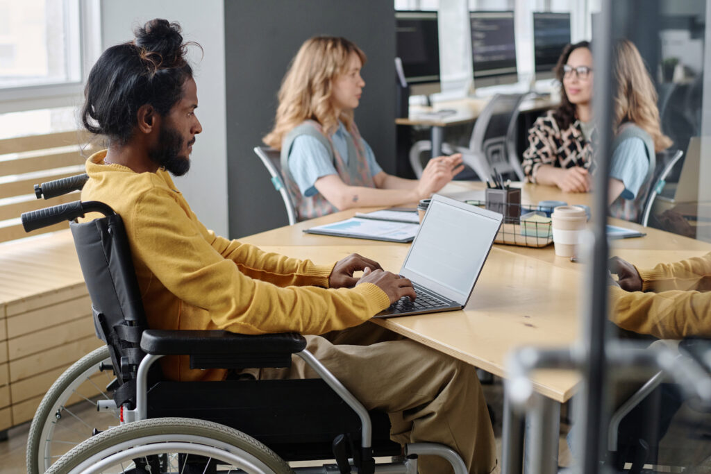 Image from the article on How to create a project's C4 model in just a few steps using an AI tool. In the image, we have a brown man with long hair tied up in a bun, he is in a wheelchair. He has a notebook resting on the table.