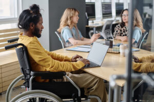 Image from the article on How to create a project's C4 model in just a few steps using an AI tool. In the image, we have a brown man with long hair tied up in a bun, he is in a wheelchair. He has a notebook resting on the table.