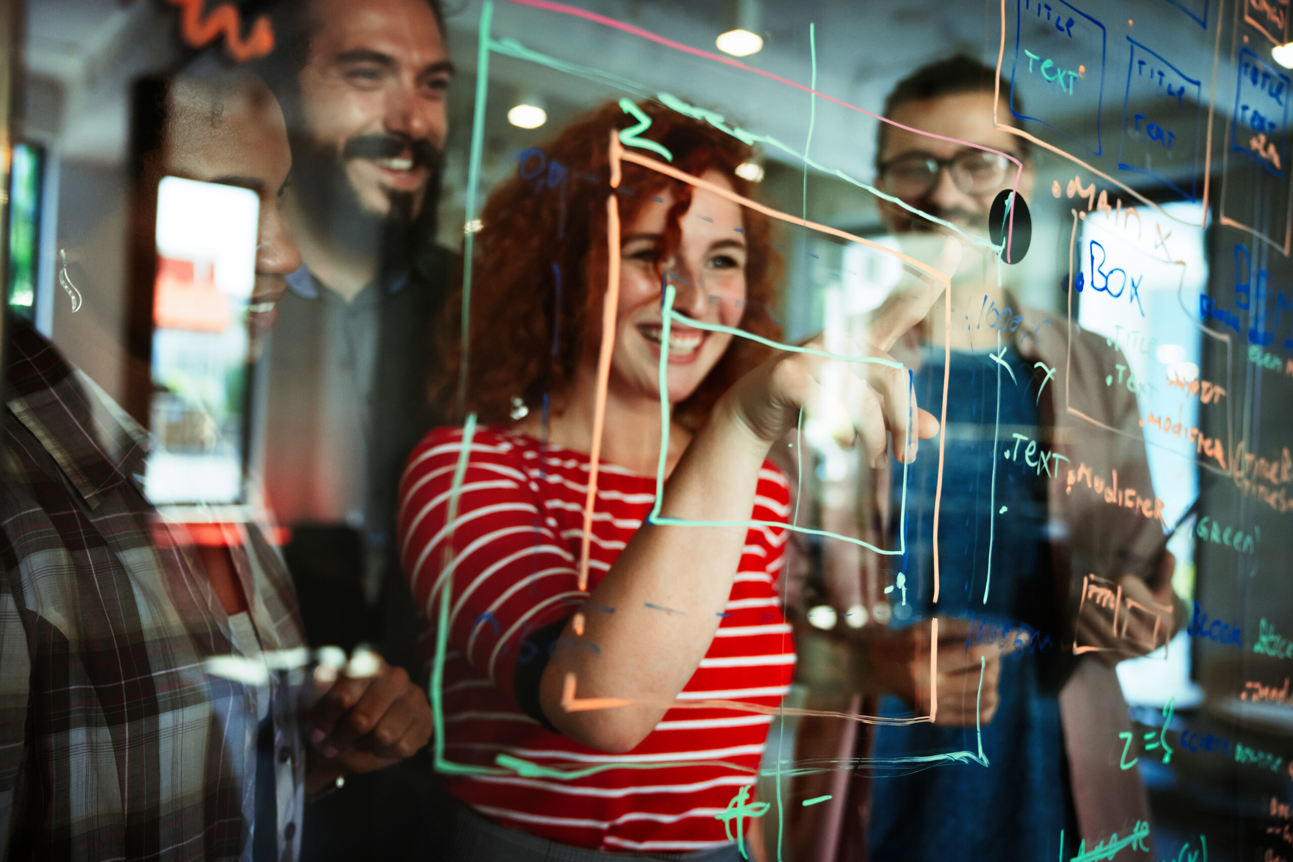 Capa do artigo sobre Evolução do desenvolvimento de software. Foto com um grupo de três programadores atrás de um vidro com anotações à caneta. Em destaque, uma mulher branca de cabelos ruivos e cacheados.