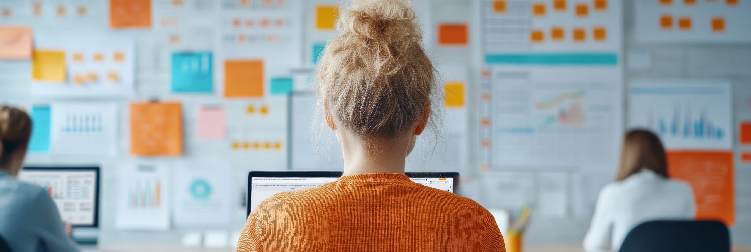 Capa do artigo sobre Planejamento de Sprints com Salesforce Unlocked Packages com Gen AI onde vemos uma mulher concentrada trabalhando no computador em um escritório moderno, cercada por gráficos e tabelas coloridas nas paredes, criando uma atmosfera vibrante e produtiva.