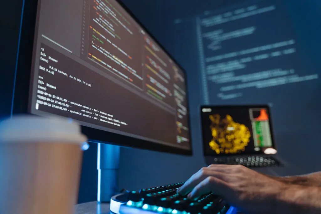 No face picture of male hands of software engineer sitting at table in front of big pc screen, typing and composing codes. Content: Evolution of Platform Engineering: a closer look at the discipline