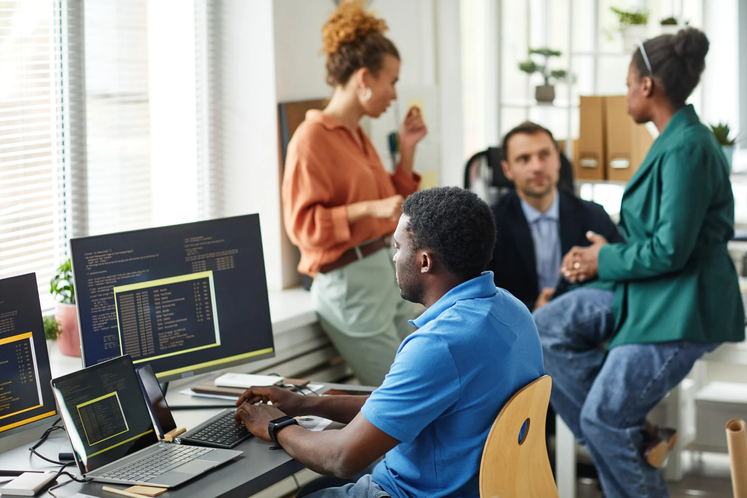 Cover image for content on trends in legacy modernization, featuring a team of developers in a room discussing, with a focus on a man in front of a computer filled with code.