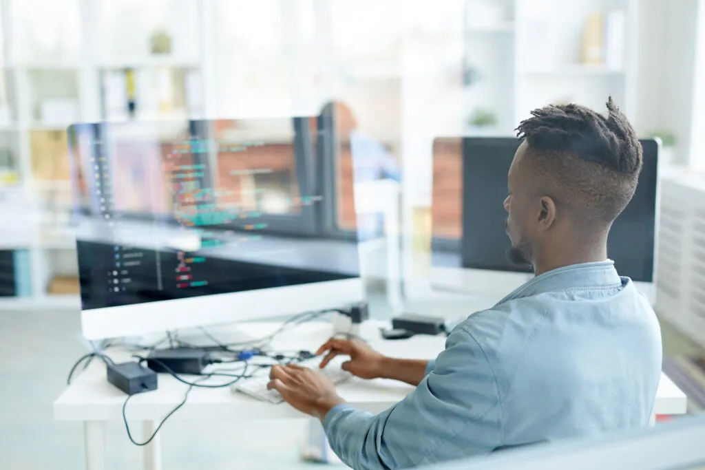 Cover image of content about Code Confidence: Improving Compliance in Platform Engineering. In it, there is a black man in front of a computer with codes on the screen.