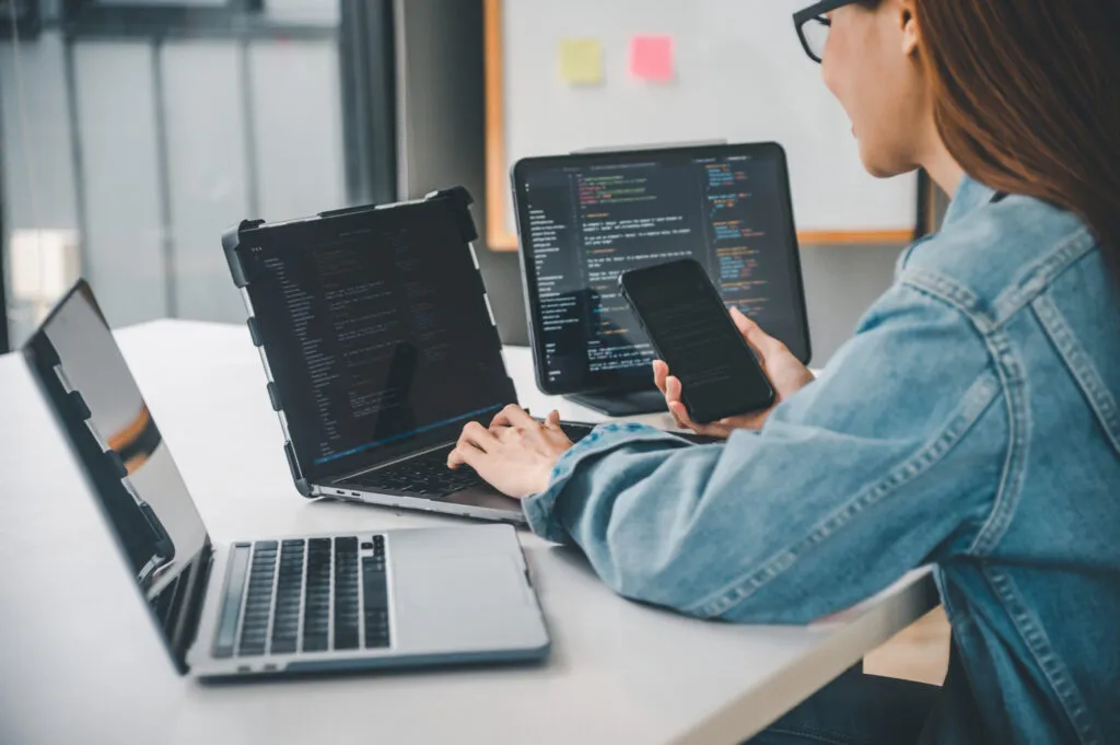 Cover image of the content on Taming Software Development Costs - Efficiency and FinOps with StackSpot Cloud Services. In the image, there is a woman facing three laptops and holding a cellphone.