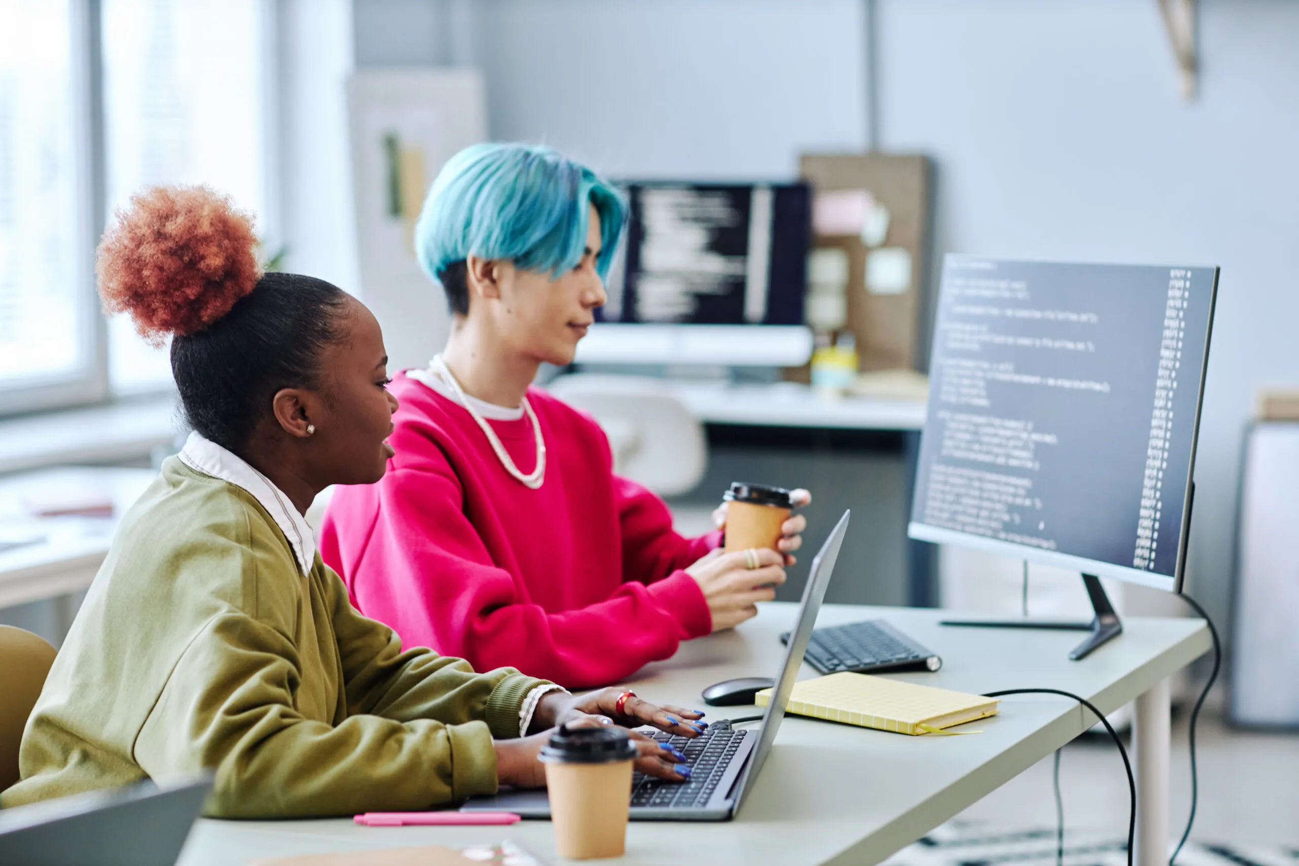 Imagem capa do conteúdo sobre Infraestrutura como código (IaC): revolucionando o desenvolvimento bancário, onde há duas pessoas jovens em frente ao monitor com códigos na tela. Uma das pessoas é uma mulher negra e ao lado um homem de cabelo curto e azul.