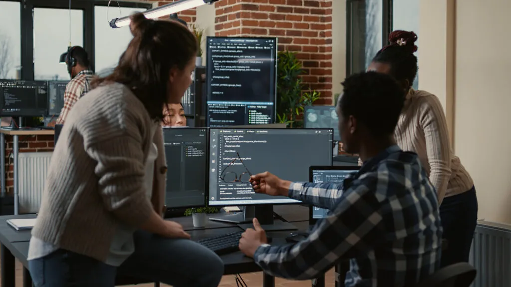 Platform teams cover. Programer sitting on desk discussing with mixed team of software developers about artificial intelligence innovation. Programmers doing teamwork looking at running machine learning algorithms.