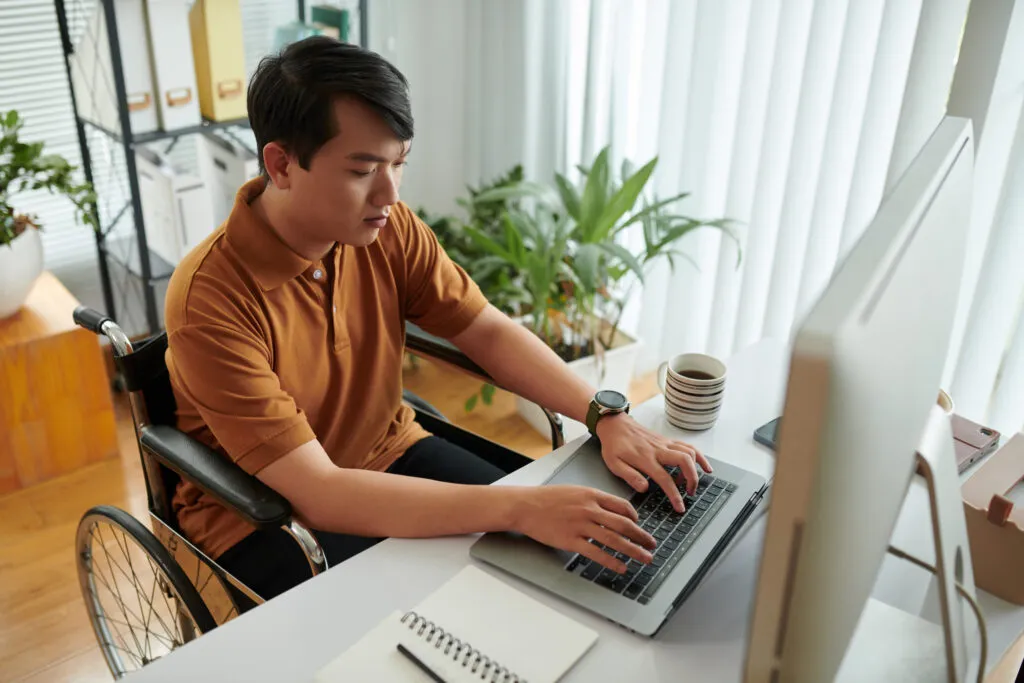 Imagem capa do conteúdo sobre Foto de um homem amarelo em uma cadeira de rodas em frente ao computador com as mãos no teclado.