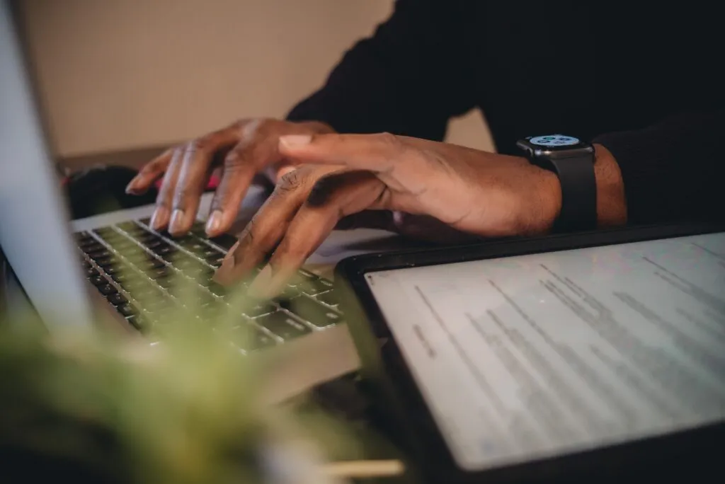 Imagem da capa do artigo "Refinamento de backlog inteligente: como uma ferramenta de AI potencializa a gestão de produto" com um homem negro sentado em frente ao computador com as mãos sob o teclado.