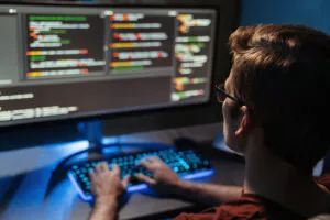 Capa do artigo Engenharia de plataforma e modernização: desafios, aprendizados e resultados. Na foto, um homem branco de cabelos claros e curtos, usando óculos de grau, está em frente a um monitor que exibe códigos. O homem está com as mãos sob o teclado.