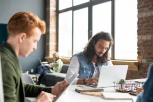 Capa do artigo Como fazer Diagramas Mermaid utilizando Quick Commands da StackSpot AI. Na imagem, um homem de cabelos compridos e barba castanhos está em frente ao notebook, que está na mesa.