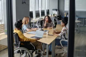 Cover of Gartner's Top Strategic Technology Trends for 2025. Three multi-ethnic women and indian man in wheelchair having business meeting at desk in office.