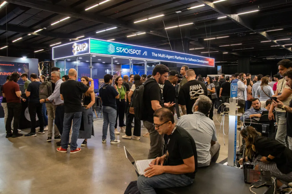 Image of the Zup stand at the StartSe AI Day event. In the foreground, we have people standing and sitting, in the background we have the stand with a screen with Zup and StackSpot AI The Multi-Agent Platform of Software Development.