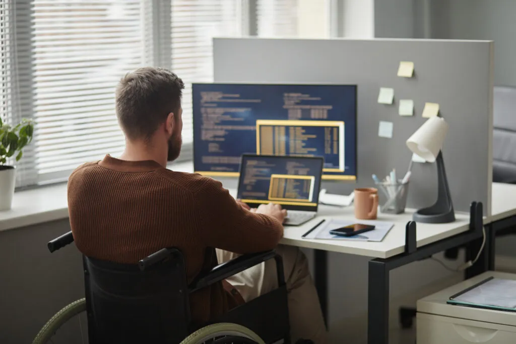 Cover of the article on “Intent Alignment”. The image shows a white man with short, light hair, sitting in a wheelchair in front of a desk. On the desk, there are several monitors displaying codes.