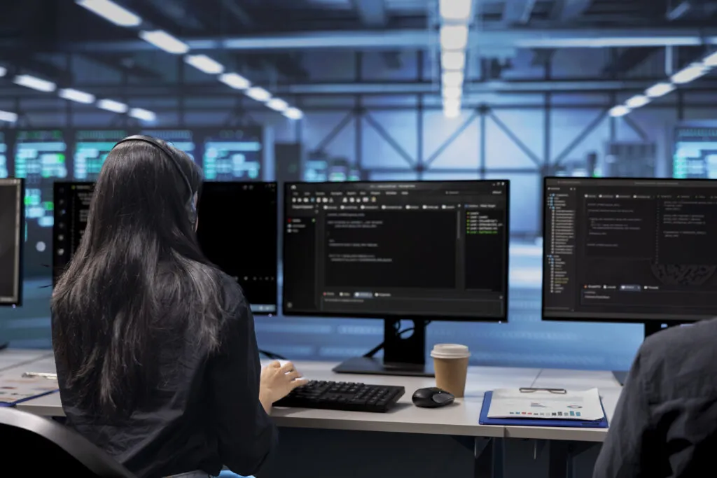 Cover of the article benefits of a multi-agent AI platform. In the image, there is a long-haired person sitting back in an office chair, in front of which is a monitor displaying code.