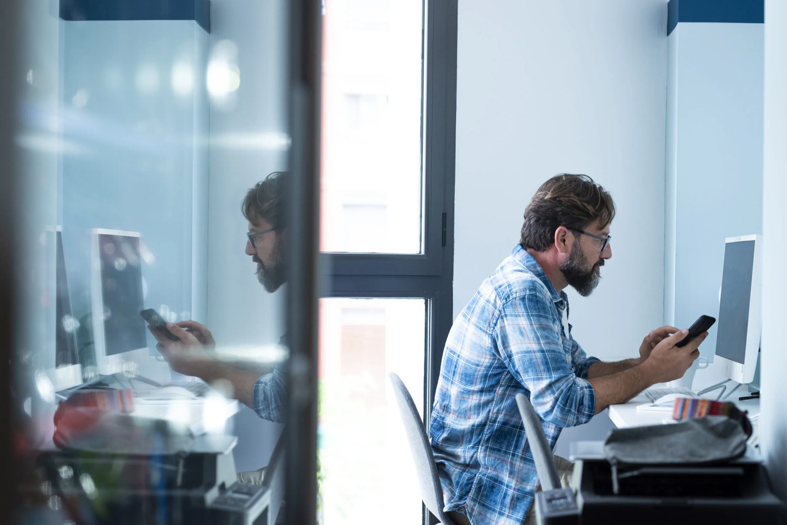 Cover image for the content about best practices for legacy modernization, featuring an adult businessman working in an office with a mobile phone and a desktop computer. Work and technology.