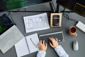 Capa do artigo sobre de IA responsável. Na imagem, temos a visão de cima de uma mesa de escritório, com notebook, monitor, celular, café e mãos em cima de um teclado.