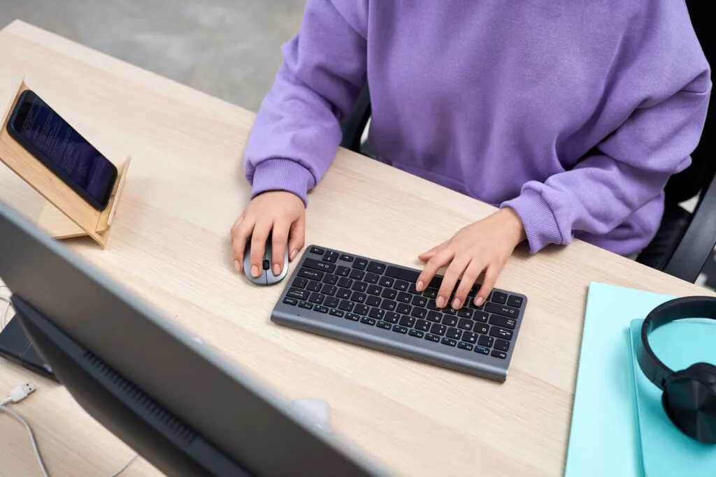 Cover of the article on the documentation migration case. The image shows a white woman wearing a purple sweatshirt with her hands under a keyboard and mouse at an office desk. The photo is taken from above.