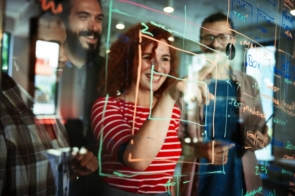 Cover of the article on the evolution of software development. The image shows a group of people behind a glass with notes in pen. A white woman with curly red hair stands out.
